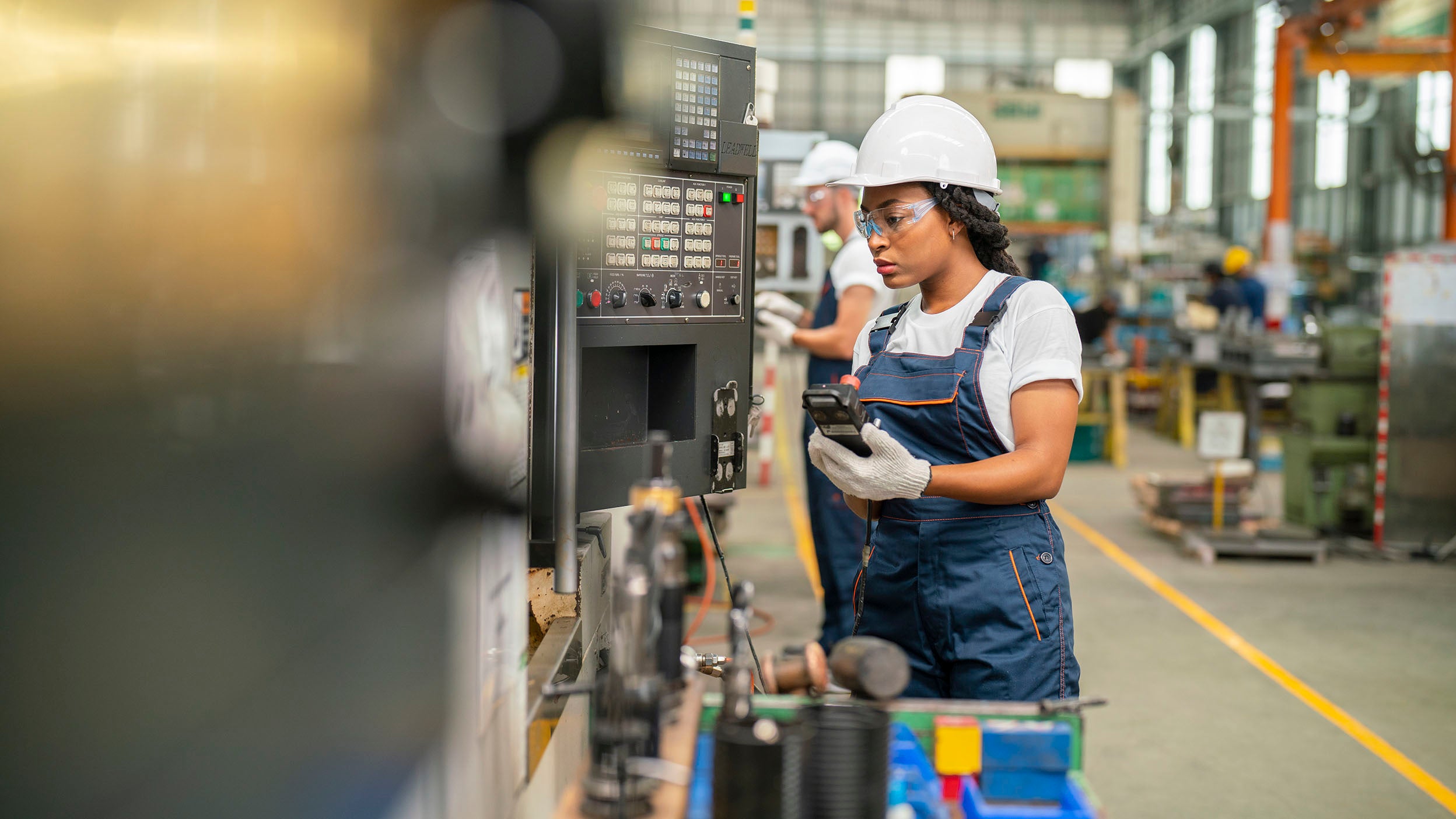 Female apprentice engineer working with CNC machine in factory