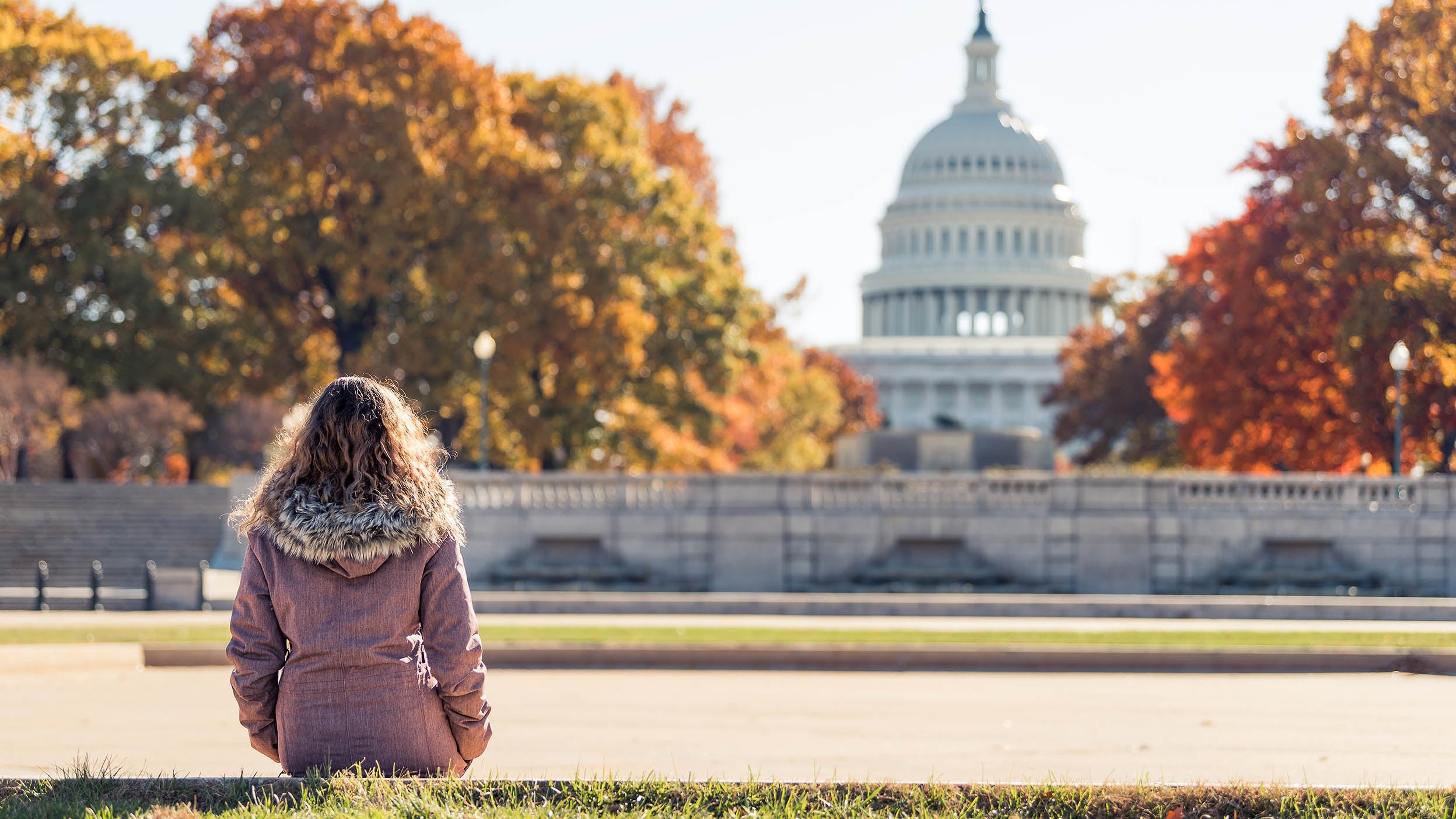 A woman in a coat looking at the US Capitol Building