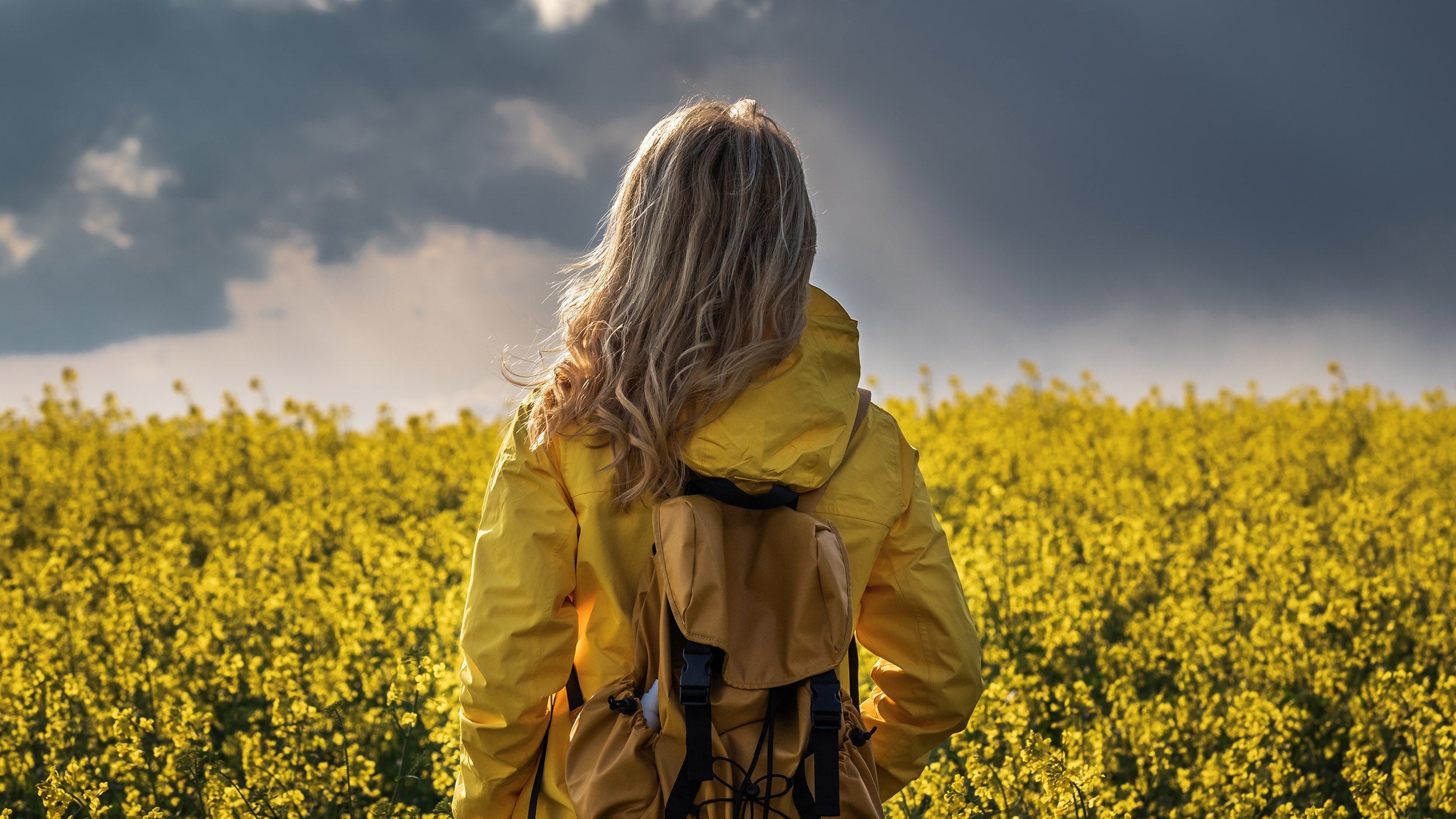 Woman looks out to field with sunlight peaking through rain clouds.