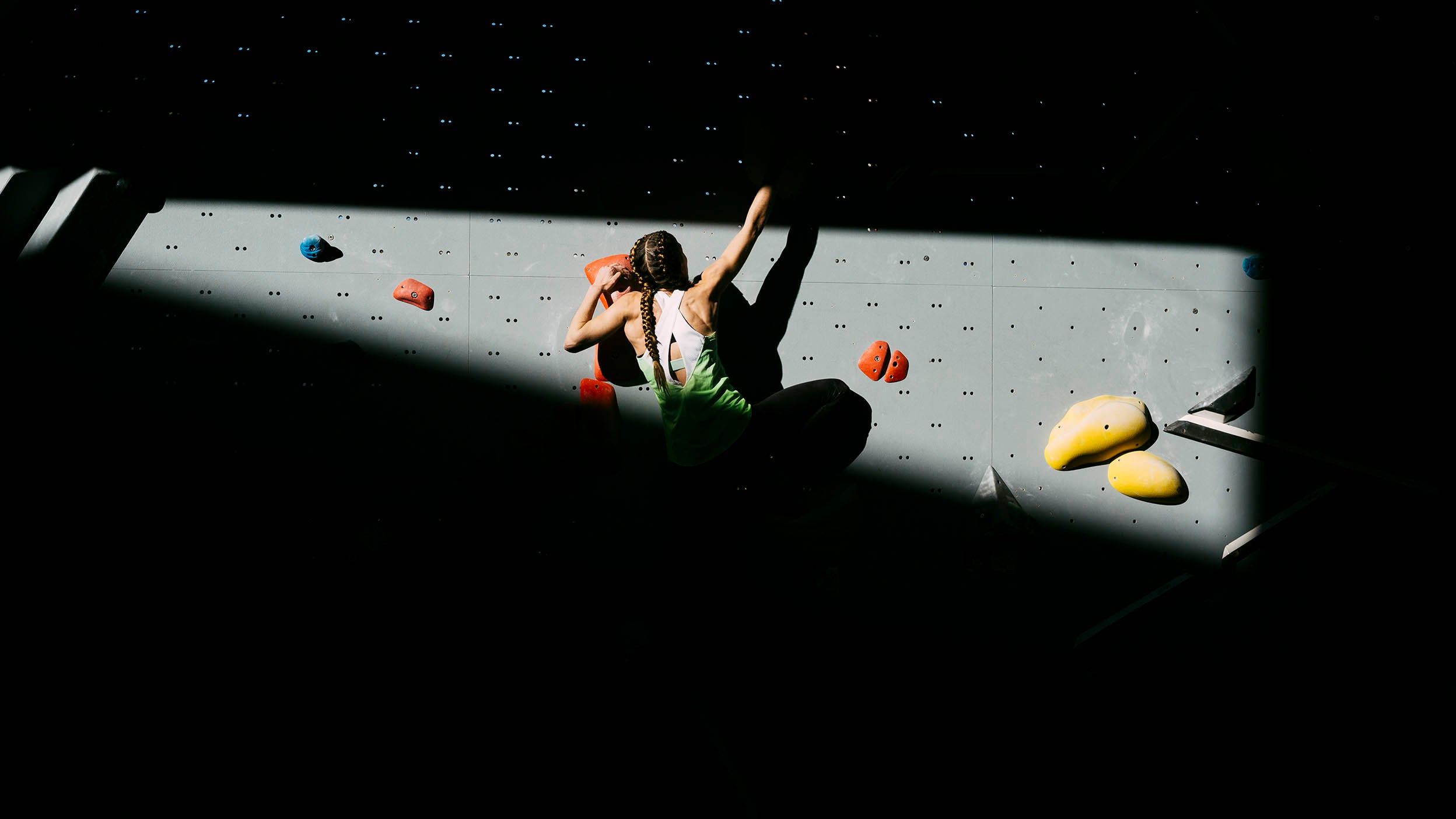 Climber making her way up a rock wall, with heavy shadows above and below her.