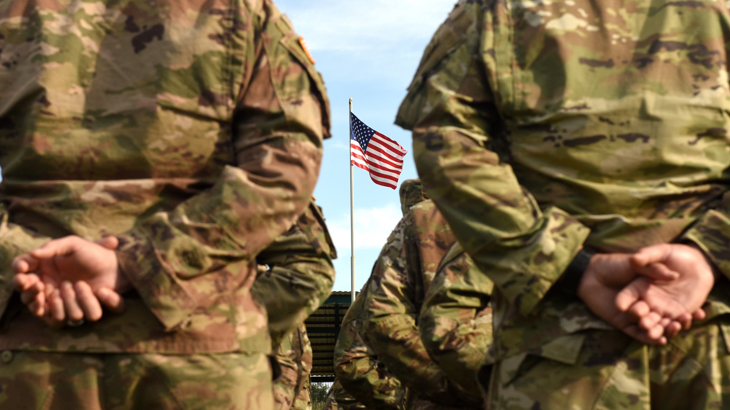 US military members stand in front of the US flag