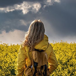 Hiking%20woman%20standing%20in%20field%20and%20looking%20at%20cloudy%20sky