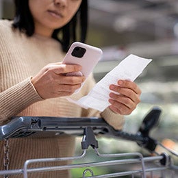 A%20woman%20examining%20a%20list%20while%20using%20a%20smartphone%20at%20the%20supermarket