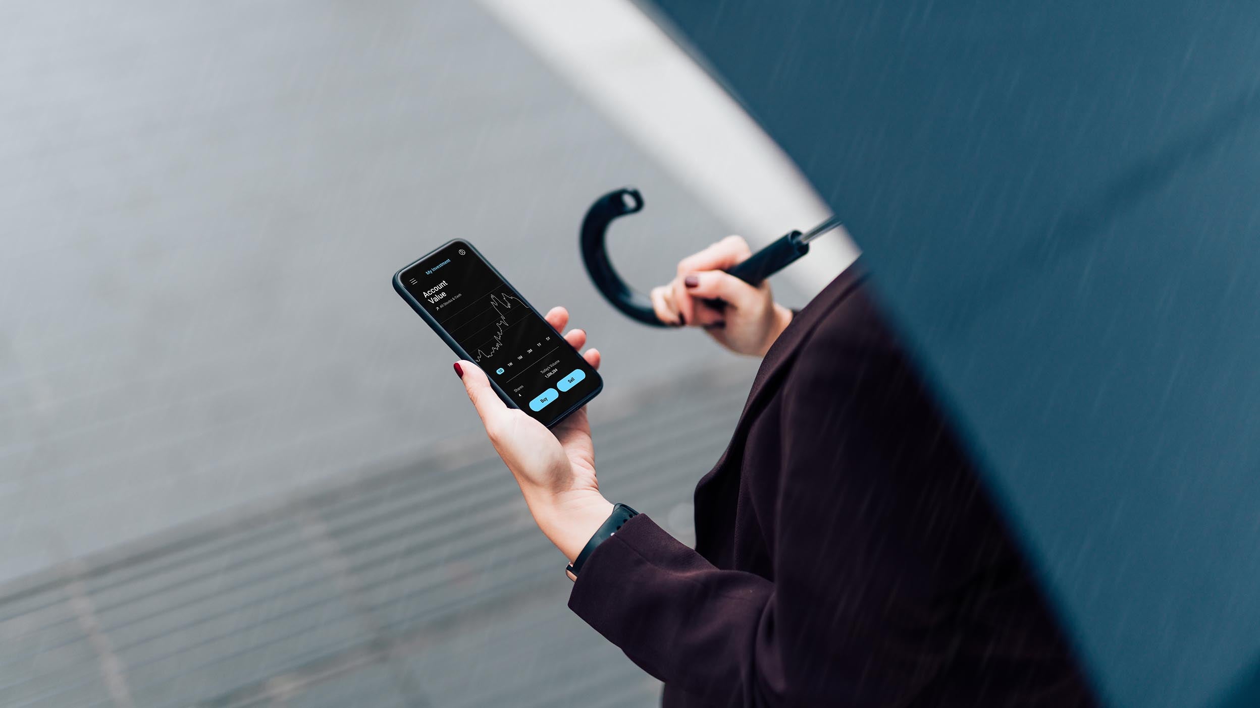 High angle view of a businesswoman using mobile app checking financial data on smartphone, holding an umbrella, walking on the city street in the rain. Insurance protection concept. Business on the go concept.