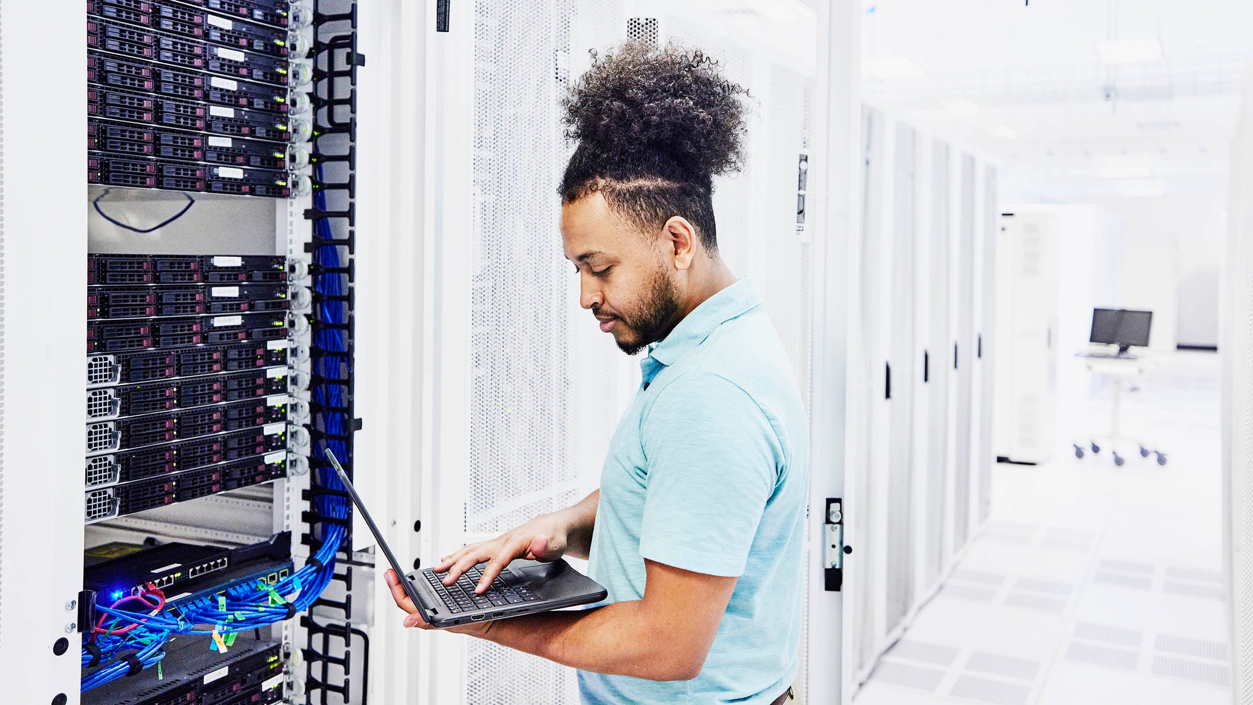 Young technician pictured working in a type of data center that cybersecurity companies featured among the Invesco QQQ holdings help protect.