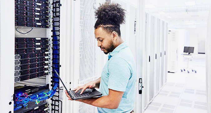 Young african american male technician monitors an electrical grid system like those at cybersecurity companies to invest in with Invesco QQQ.