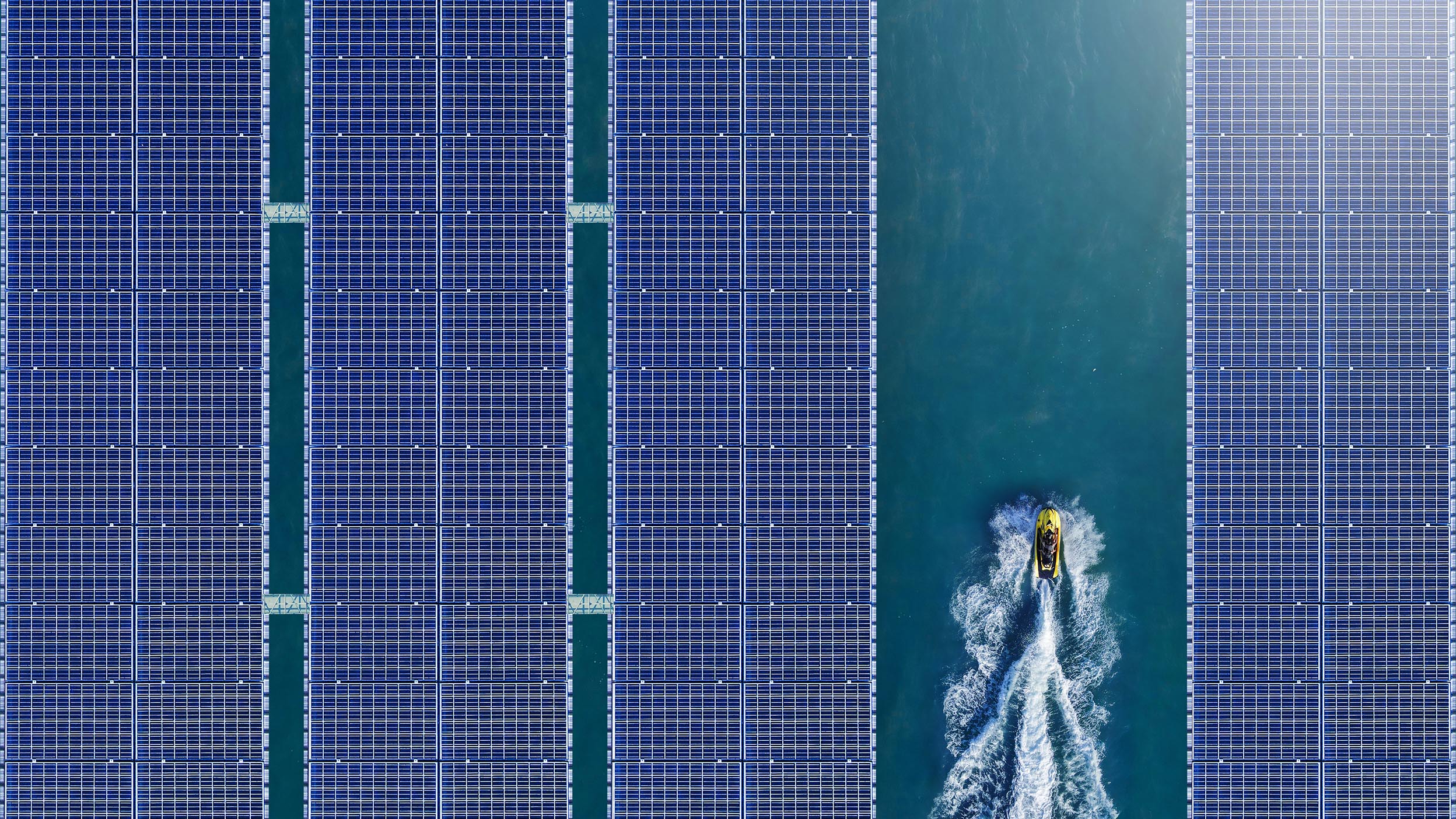A boat rides through a row of solar panels over a body of water, representing one of the many innovative ways that companies within Invesco QQQ ETF are harnessing energy.