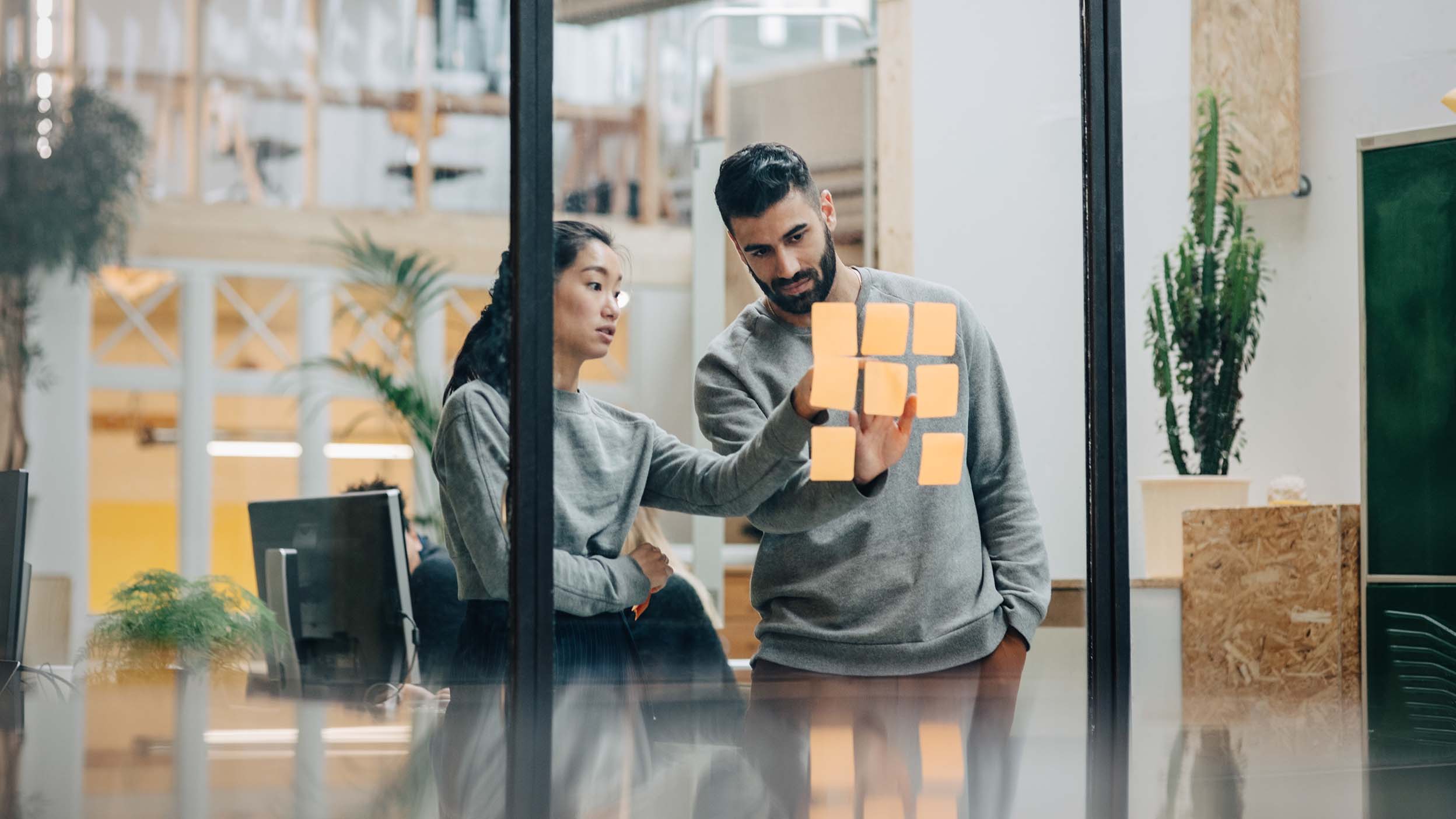 Business persons with sticky notes on glass wall in office discussing research and development topics as innovated by Invesco QQQ holding companies.