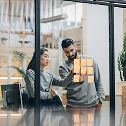 Business%20persons%20with%20sticky%20notes%20on%20glass%20wall%20in%20office%20discussing%20research%20and%20development%20topics%20as%20innovated%20by%20Invesco%20QQQ%20holding%20companies.