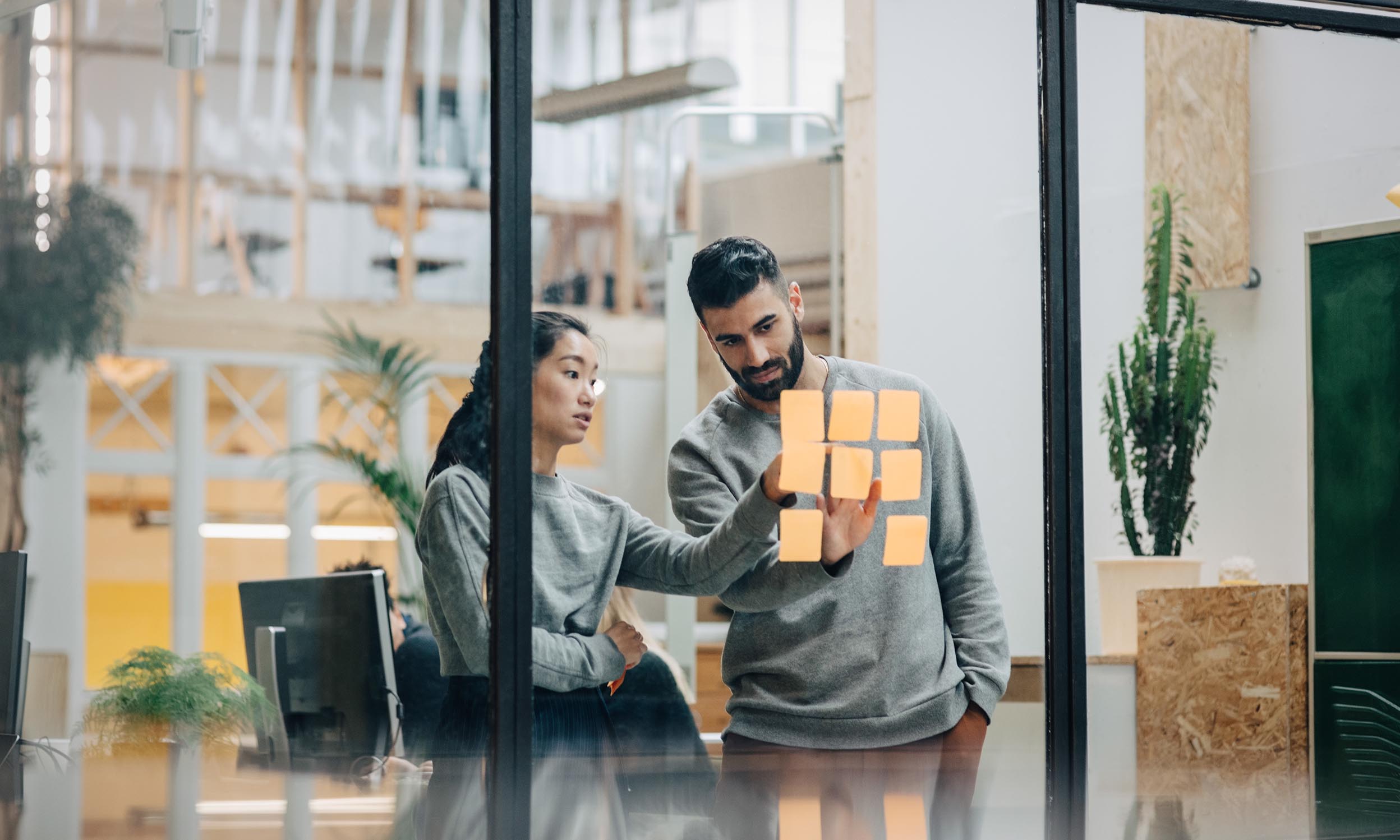 Business persons with sticky notes on glass wall in office discussing research and development topics as innovated by Invesco QQQ holding companies.