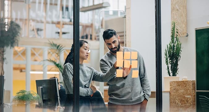 Businessman discussing with businesswoman sticking adhesive notes on glass wall in office