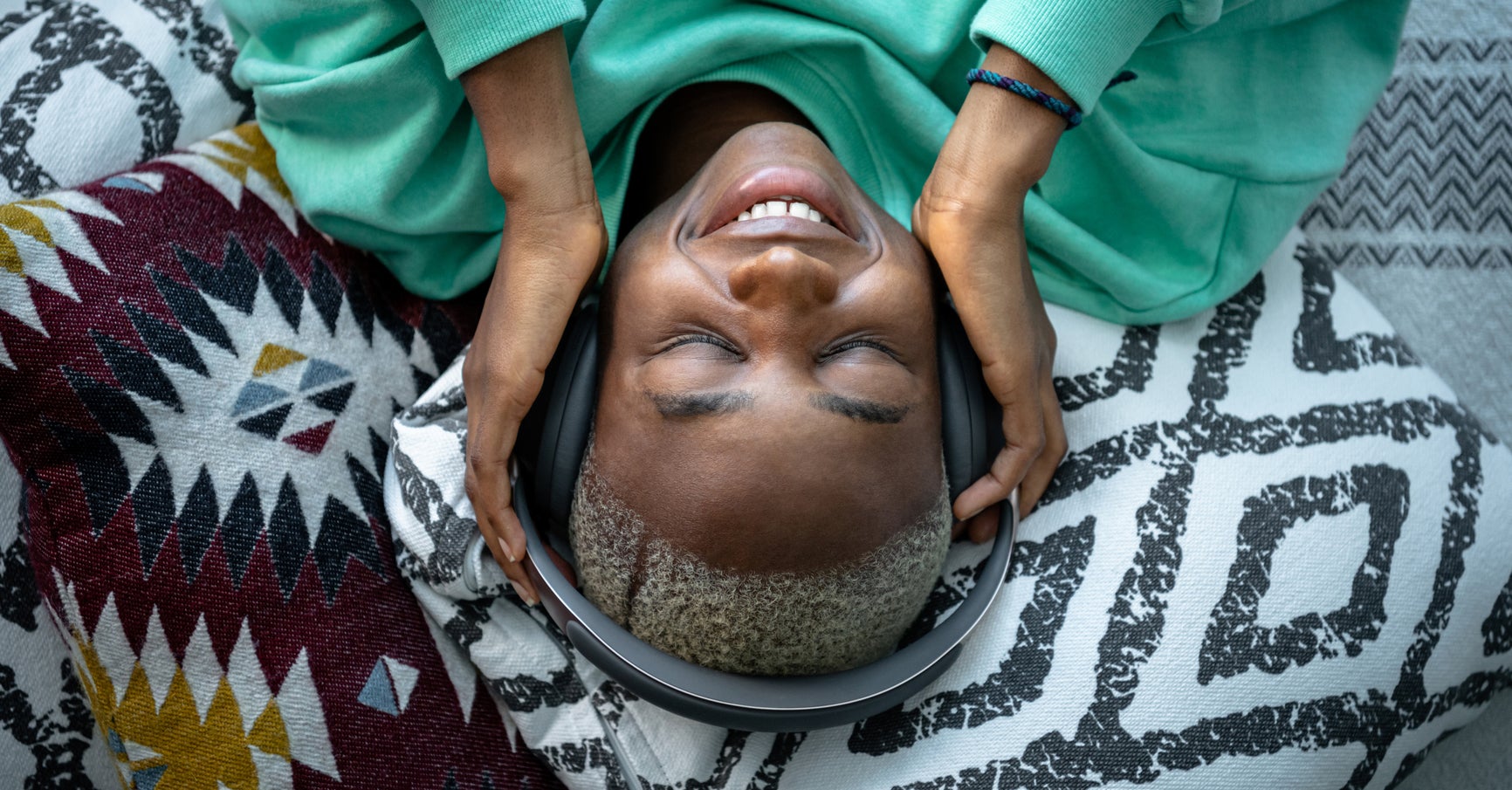 Young African woman lying on bed, smiling and listening music on headphones in the afternoon.