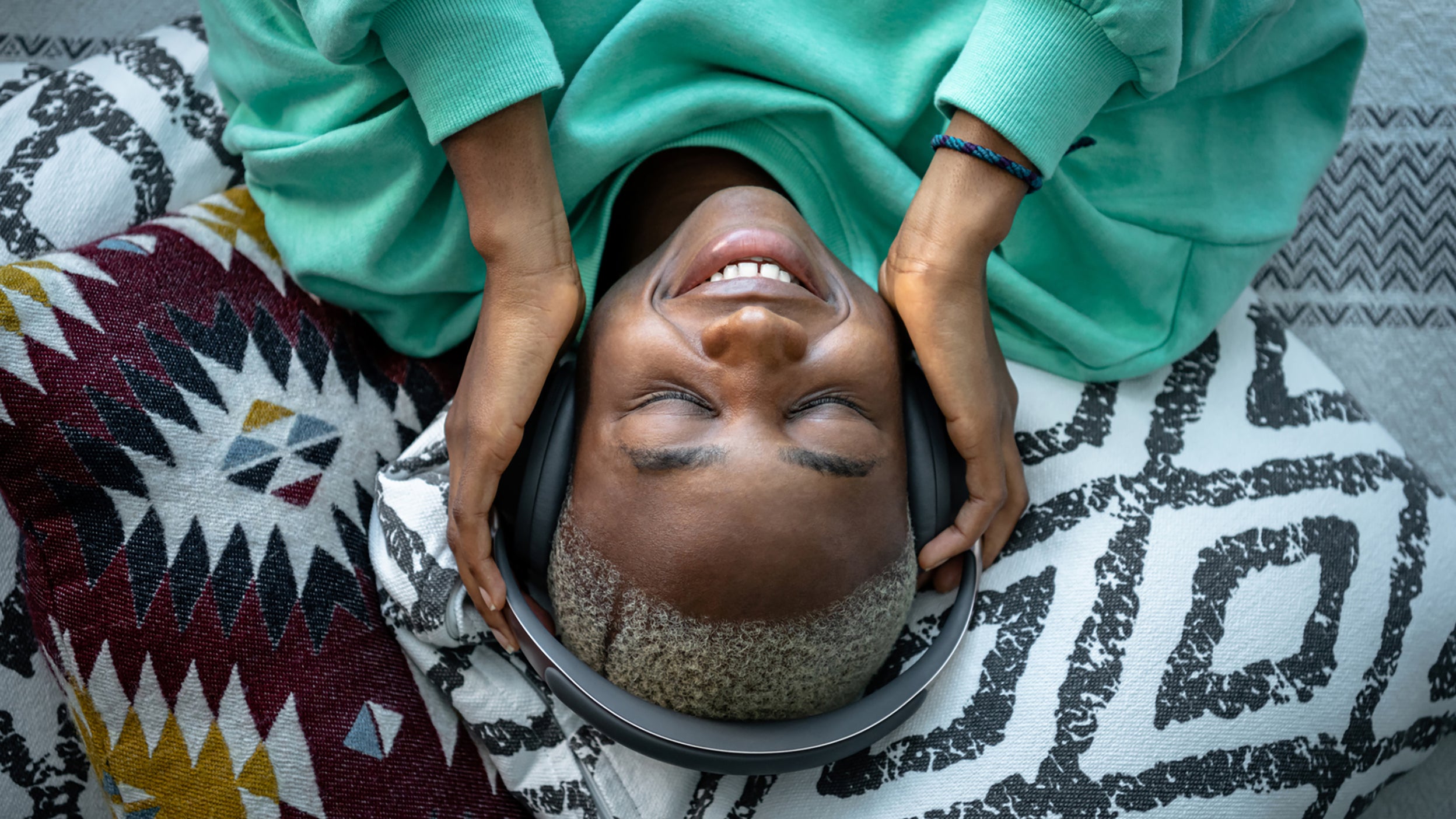 Young African woman lying on bed, smiling and listening music on headphones in the afternoon.