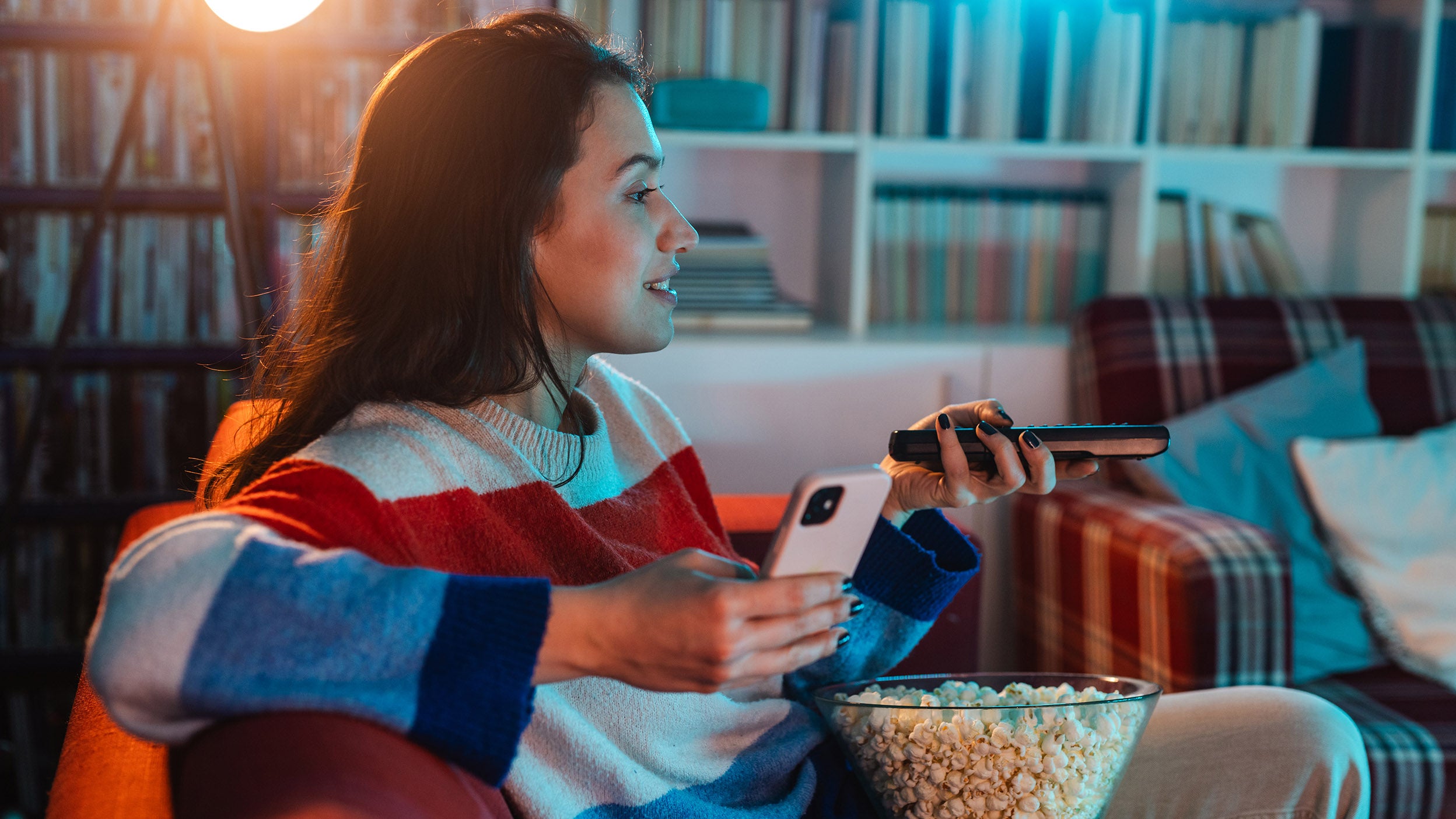 A women changes the channel on TV while also checking her phone. Invesco QQQ ETF provides exposure to many companies in the TV streaming industry. 
