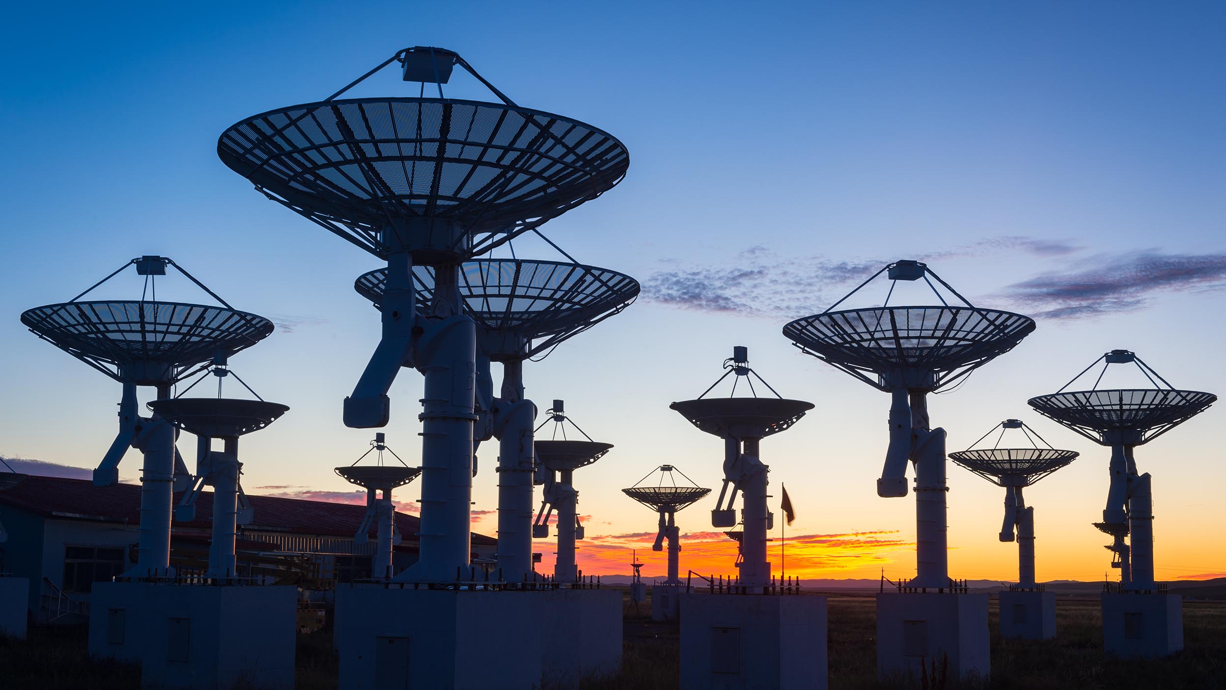 A group of satellites on the ground with a sunset behind them. These represent the telecommunications industry, a sector within Invesco QQQ ETF.