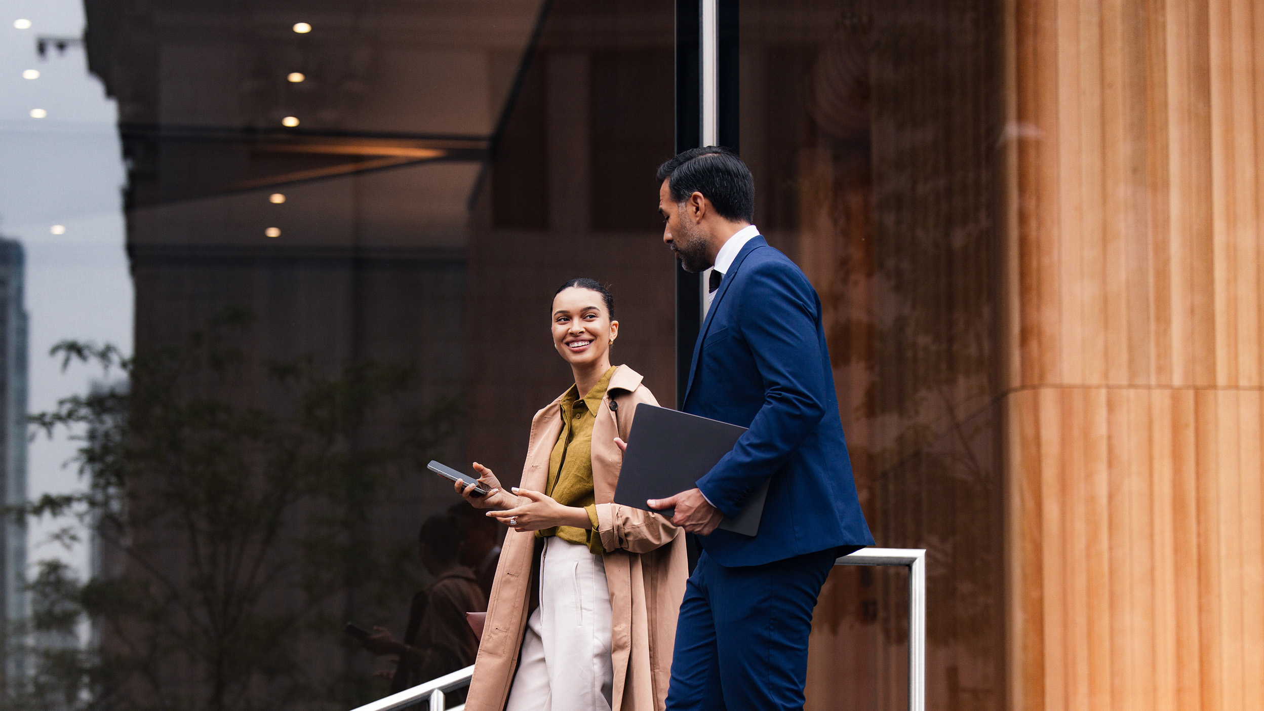 Two people walking outside an office building with laptops