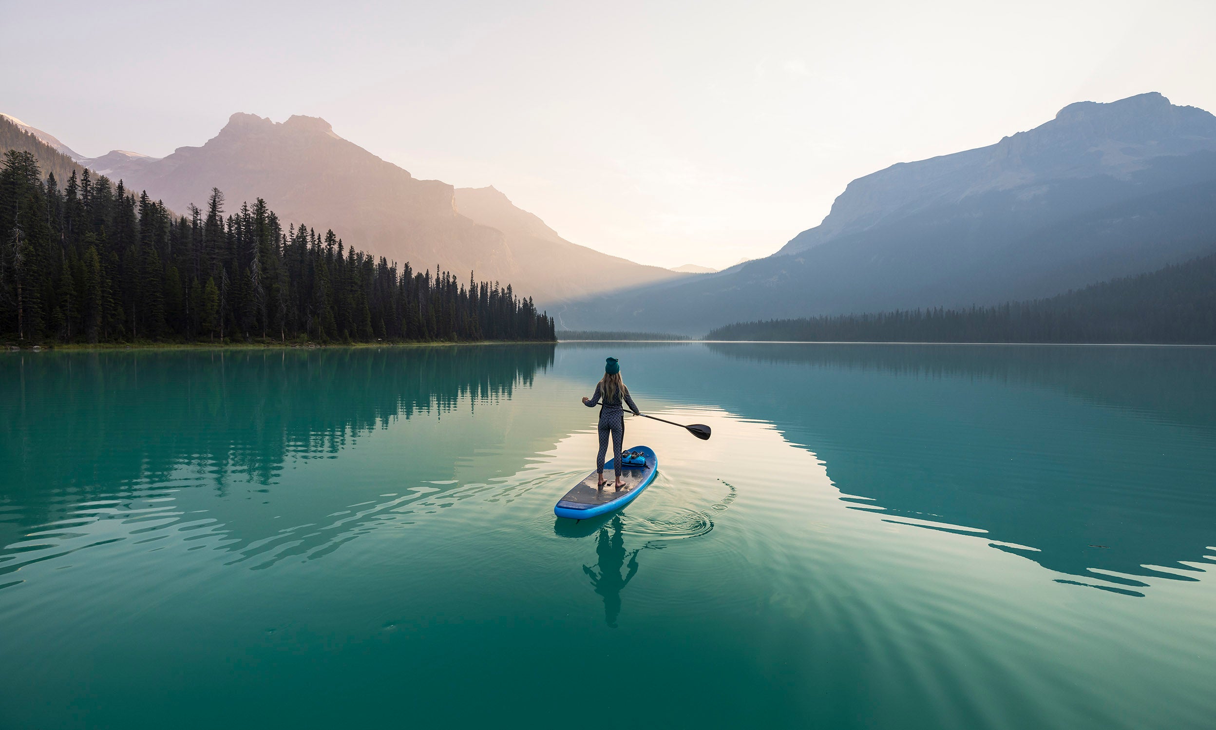 Woman standing on a paddle board in a lake looking at the mountains