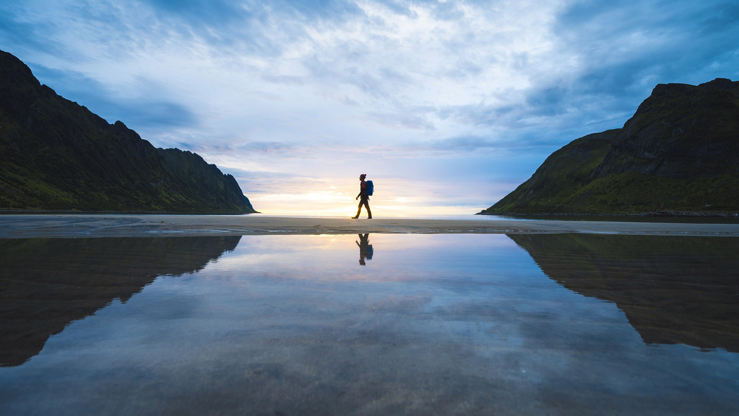 Person walking on a wide beach at sunset