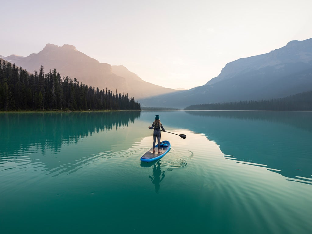 Woman standing on a paddle board in a lake looking at the mountains
