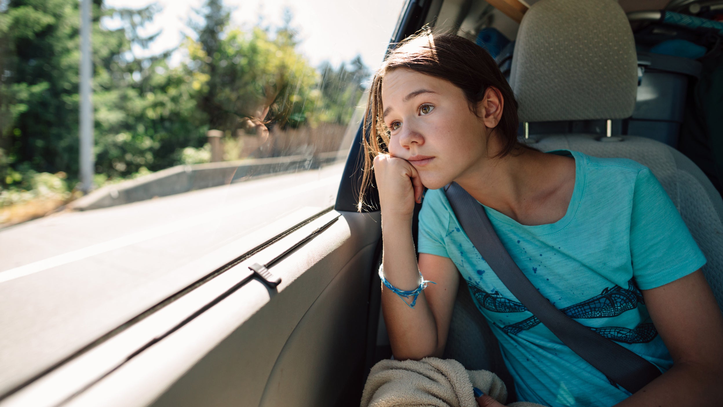 Bored kid in the backseat of a car, looking out window.