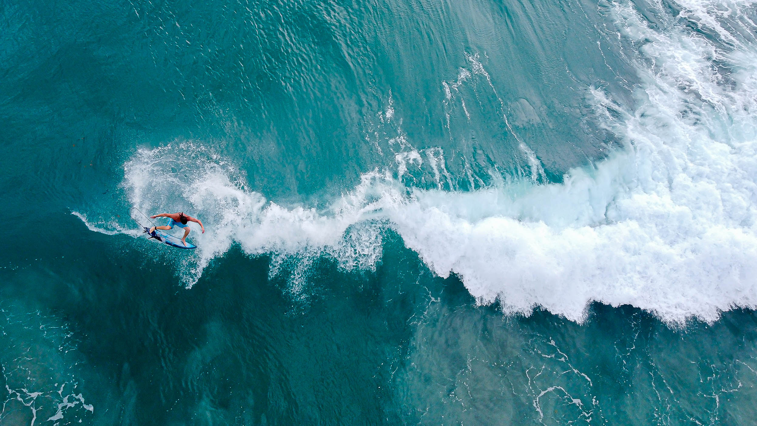 Man big-wave surfing in bright blue water.