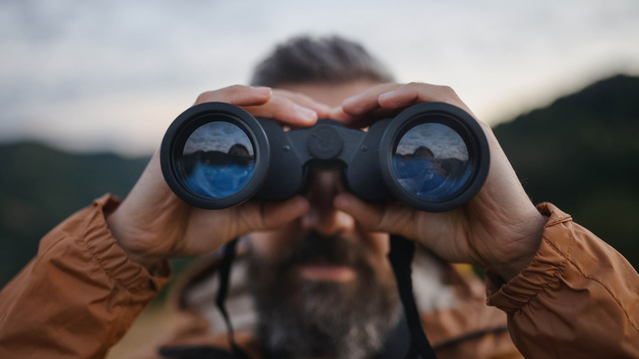 Portrait of man looking through binoculars outdoors during autumn morning.