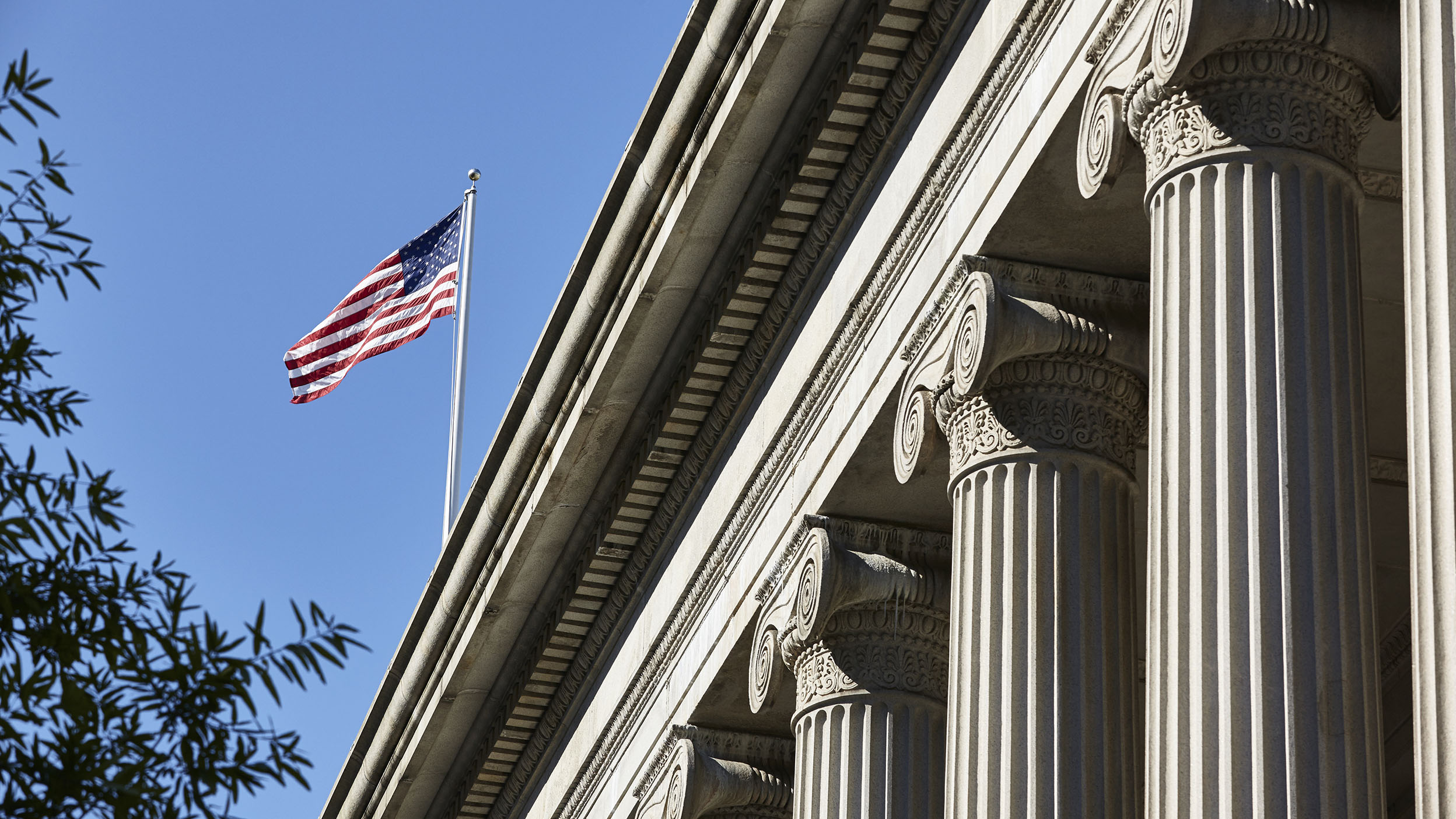 The US flag waving in the sunshine over the columns of the Treasury Departments East facade