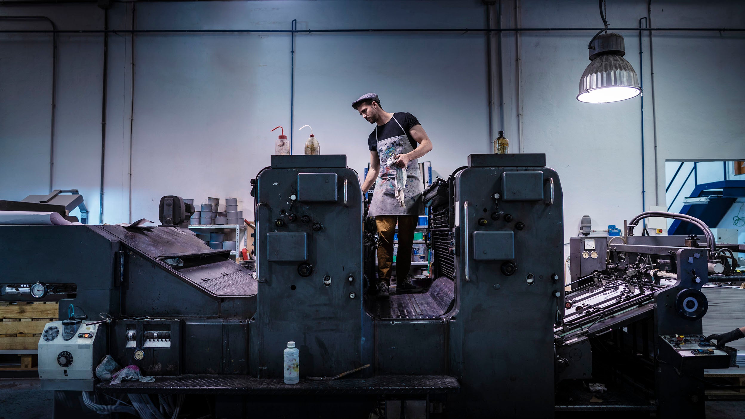 Worker operating a large industrial printing press in a manufacturing facility.