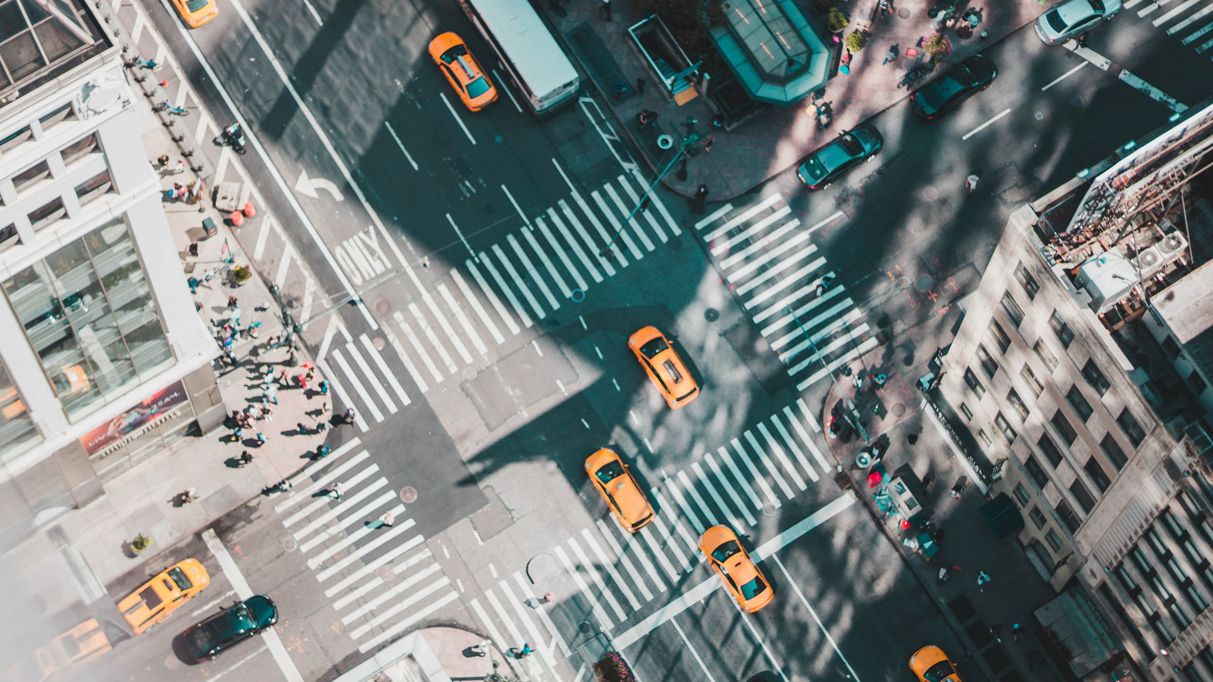 Aerial view of a bustling intersection with business people heading to meetings, surrounded by tall urban buildings casting long shadows.