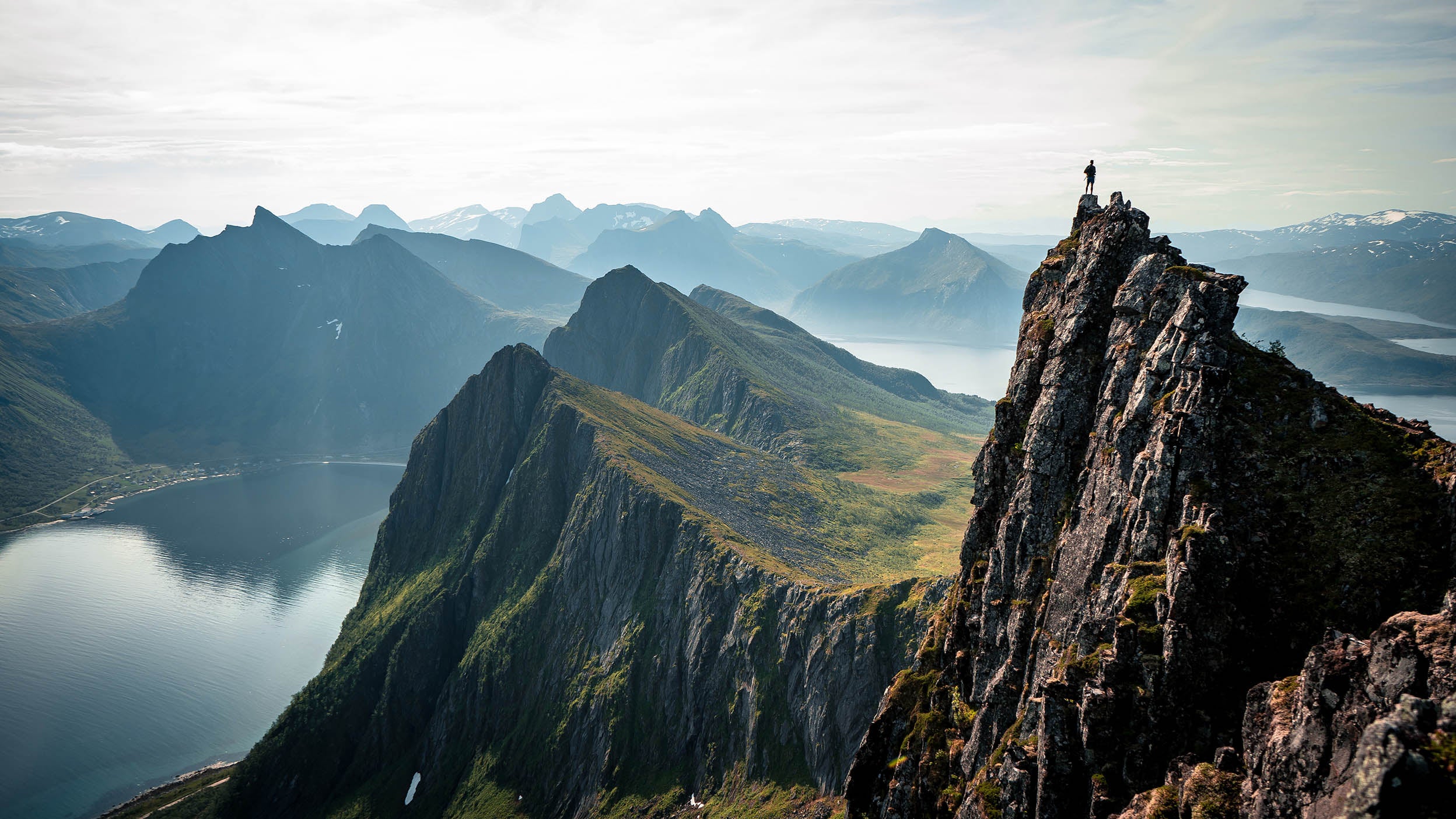 A person stands on top of a mountain looking at other mountain peaks. 