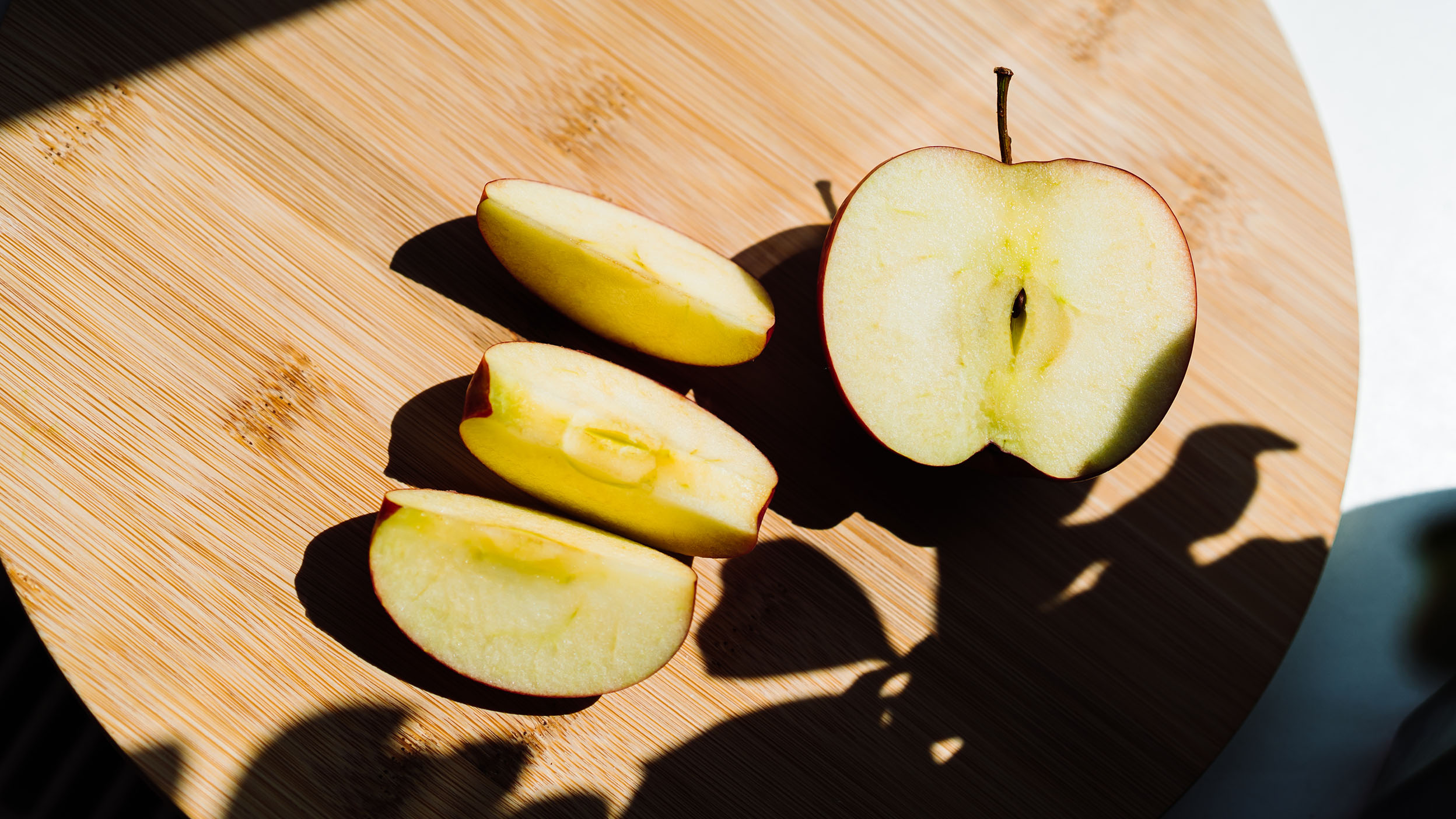 Sliced apples displayed on a wooden cutting board under bright natural lighting, creating a cozy and fresh atmosphere.