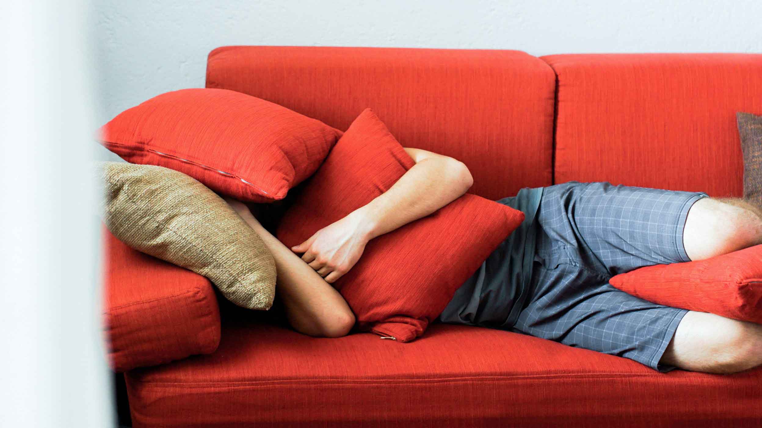 Young man is hiding under pillows in the sofa