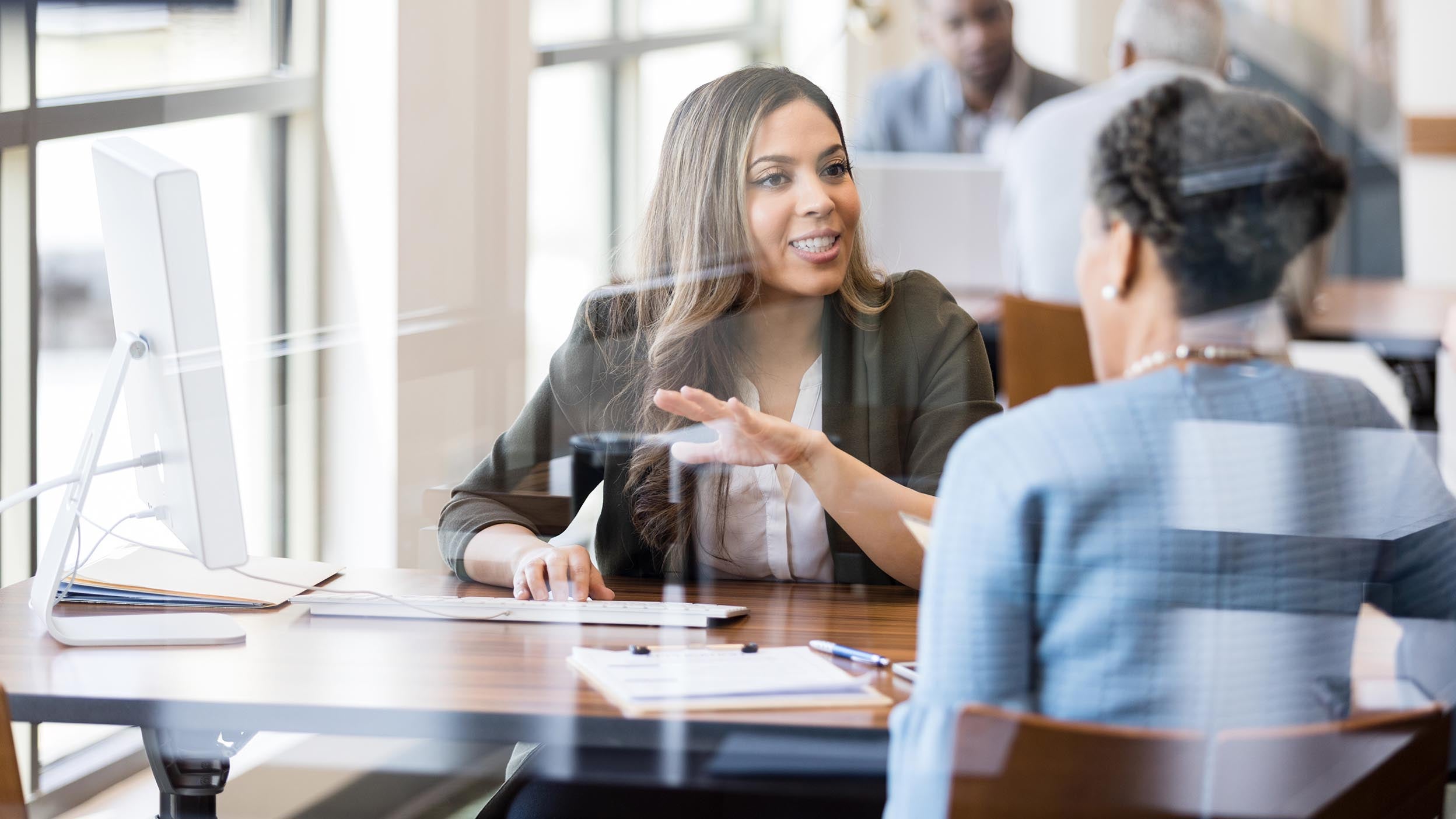 A female bank employee gestures as she explains banking services to a female customer.