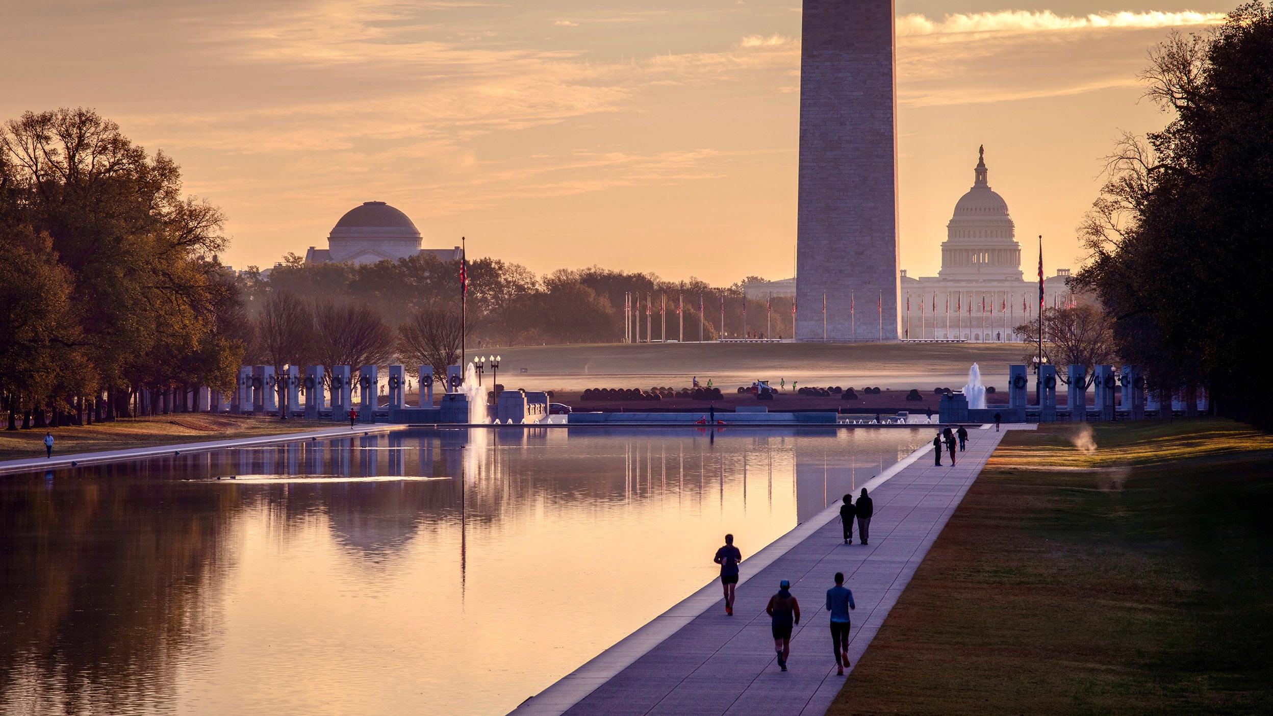 Sunrise over the Washington Monument reflected in the pool, with people walking along the path.