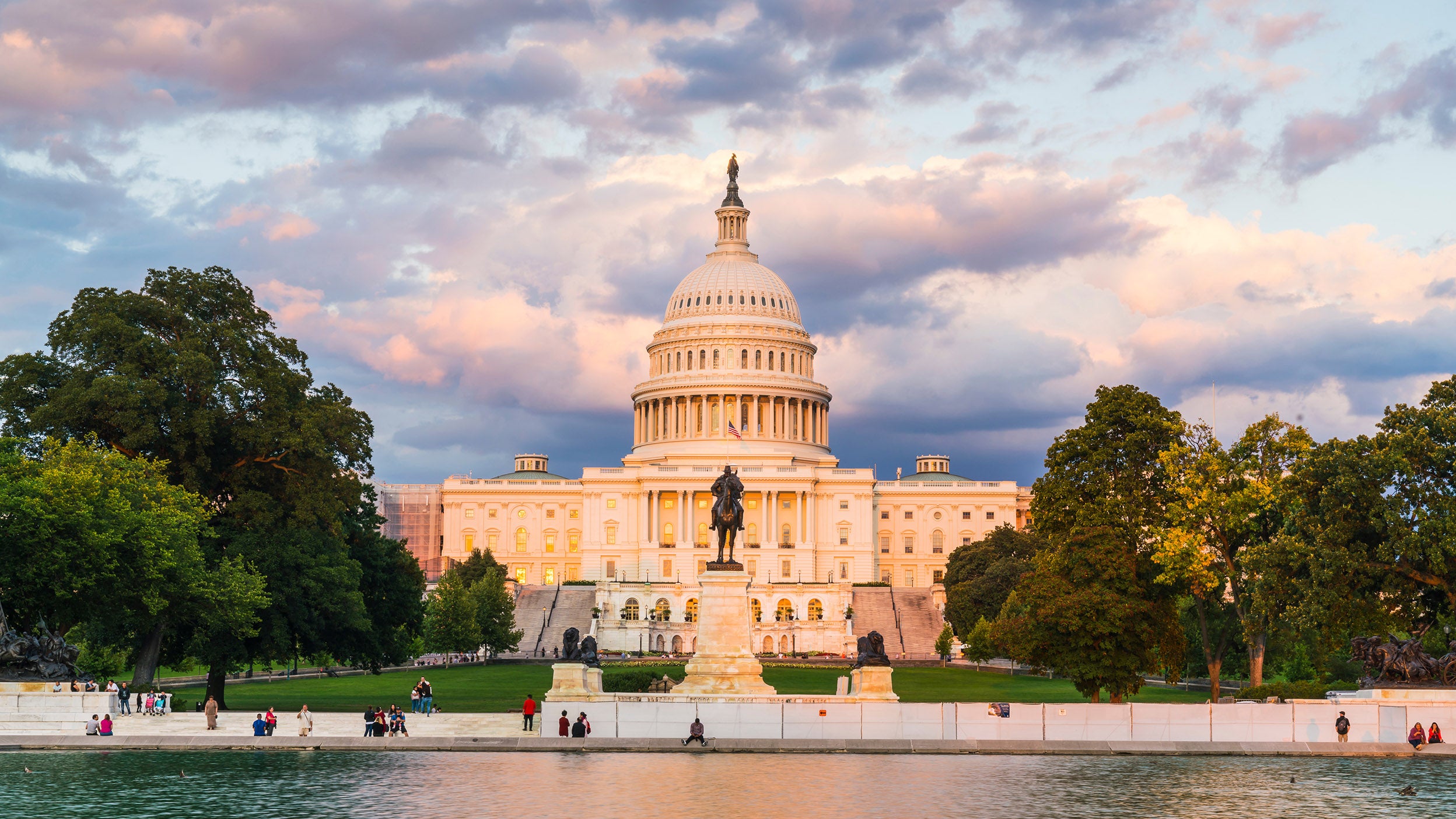 The US Capitol building at sunset with reflection in water.