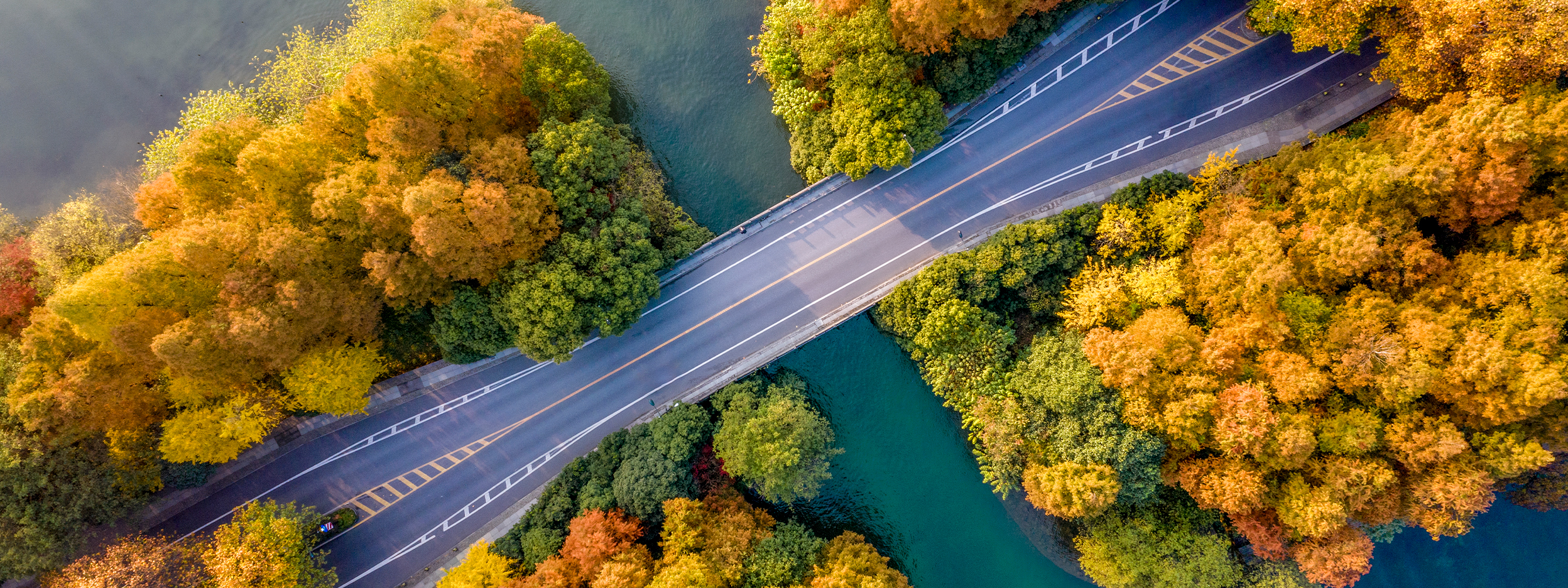 Aerial view of a bridge crossing a river surrounded by autumn trees