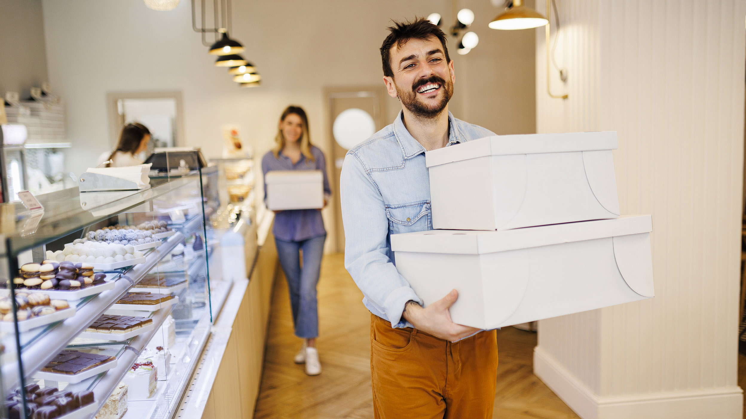 Shop worker carrying stacked boxes in a bakery