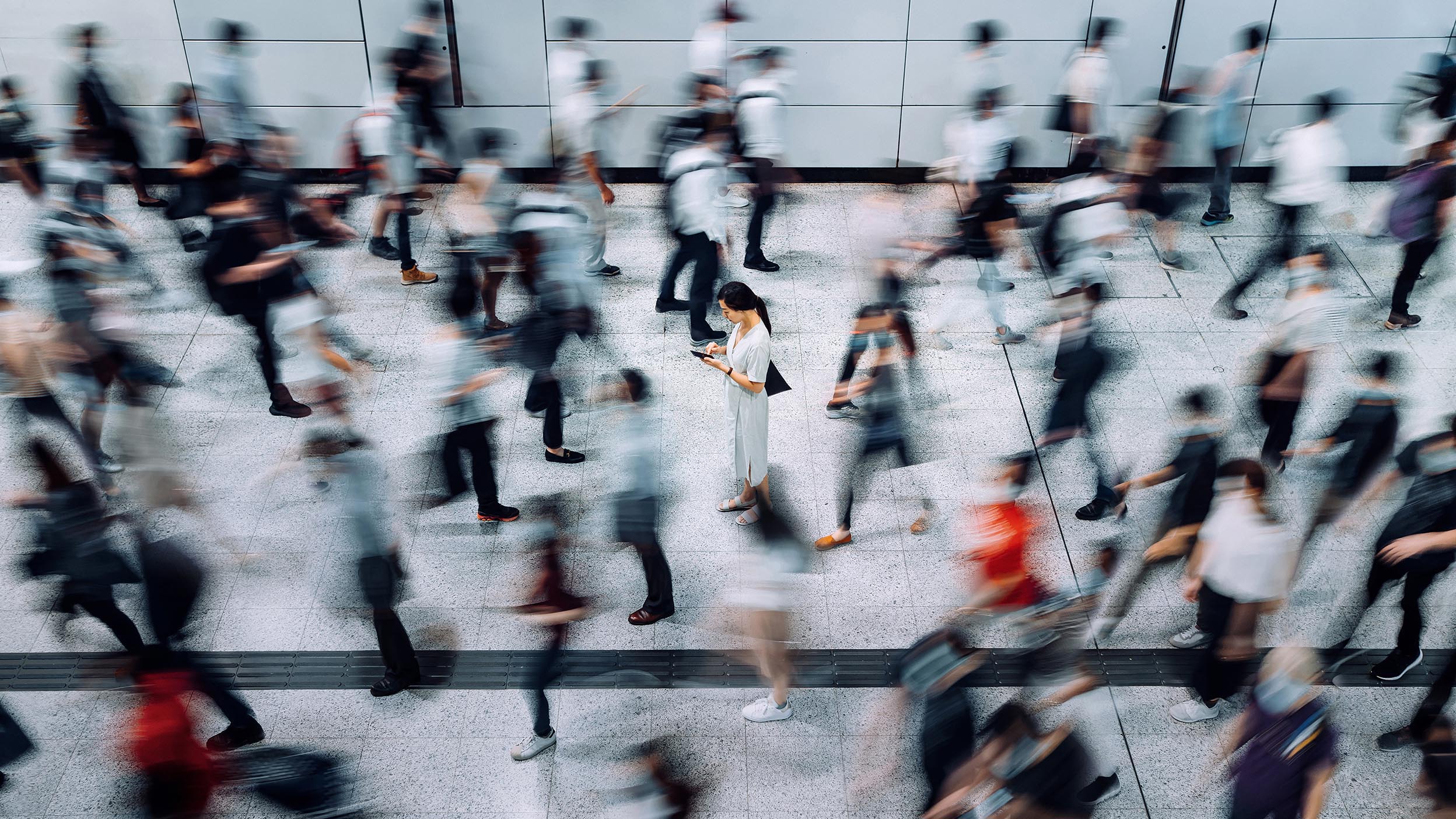 Woman using smartphone surrounded by commuters rushing by in subway station during office peak hours in the city. 