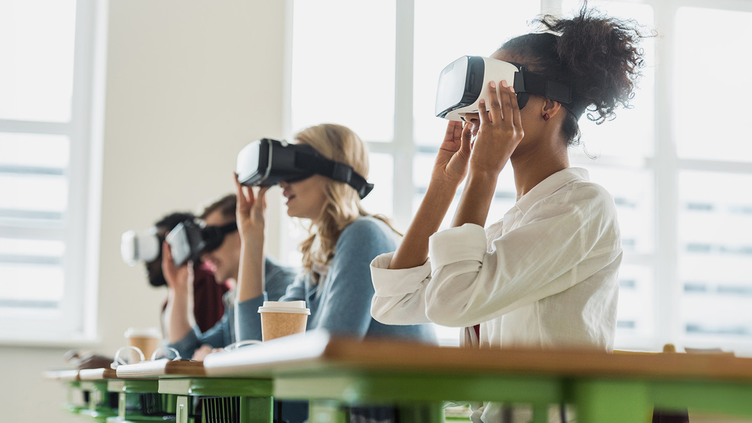 Group of college students at desks trying out VR headsets.