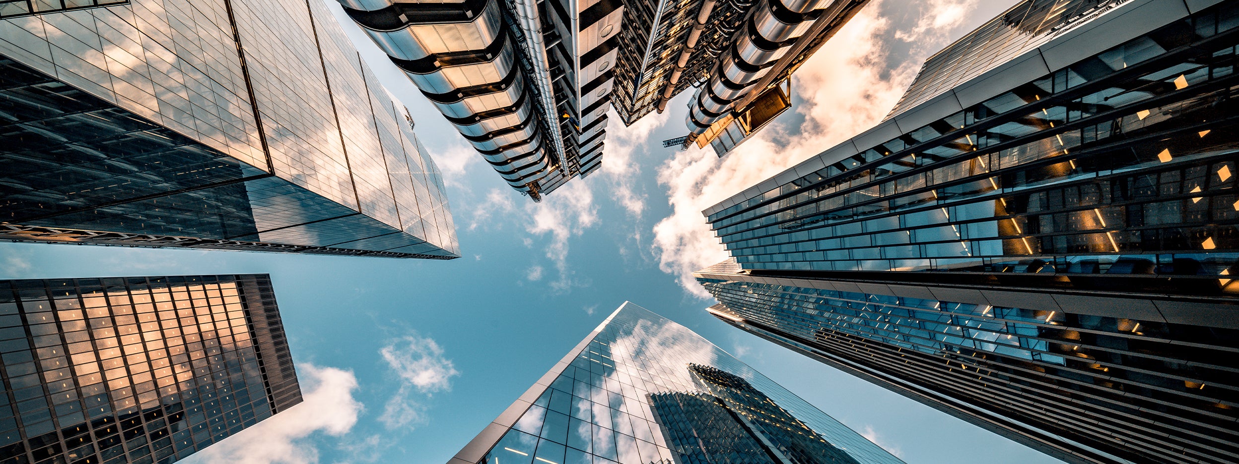 Looking up at modern glass skyscrapers against a blue sky.